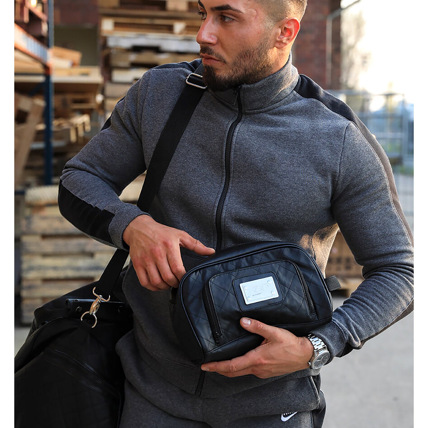 Zecplus Lifestyle Kulturbeutel Schwarz Mann in Sportoutfit vor Paletten trägt den Kulturbeutel